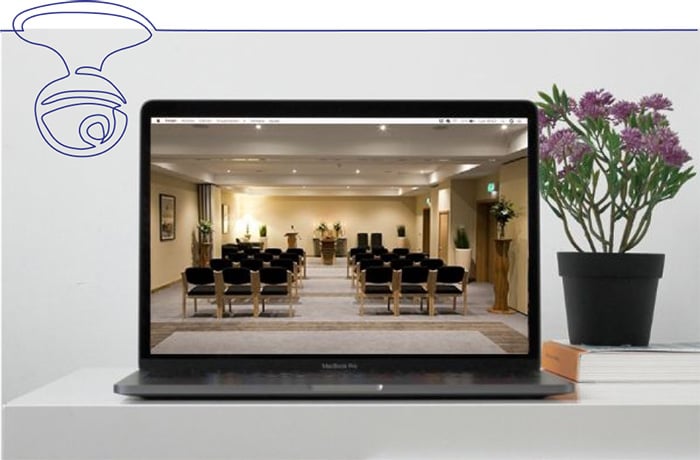 Funeral service live stream on a laptop displayed on desk with flowers and books 